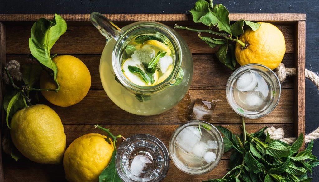Jug and glasses with homemade lemonade, ice cubes on wooden tray, top view